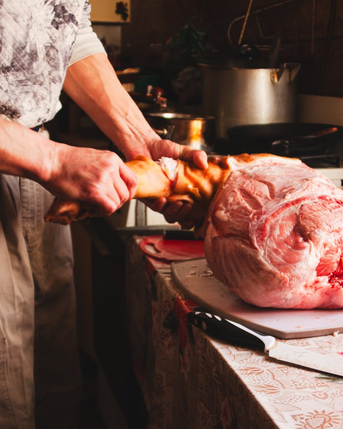 Chef skillfully butchering a raw pork leg in a kitchen using sharp cutlery.